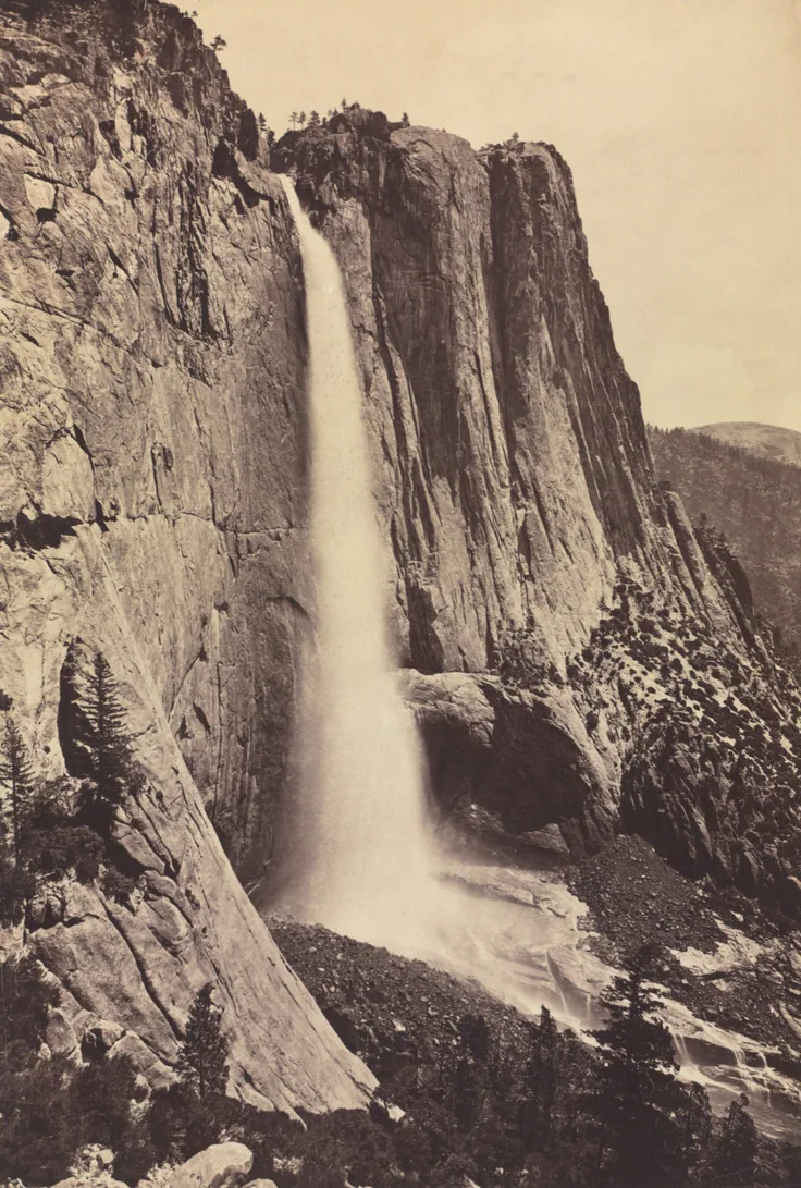 Tall vertical view of a waterfall pouring down a sheer granite wall into mist; warm sepia tones and crisp rock texture.