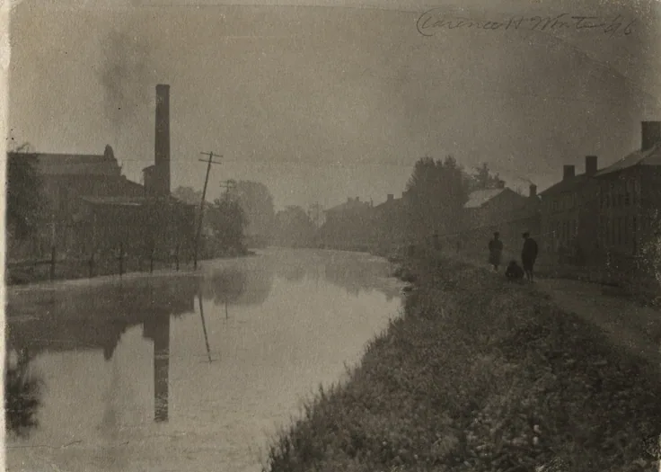 Mist over a still canal in Newark, Ohio, a smokestack and brick mills behind, two small figures on the towpath; soft grey print.