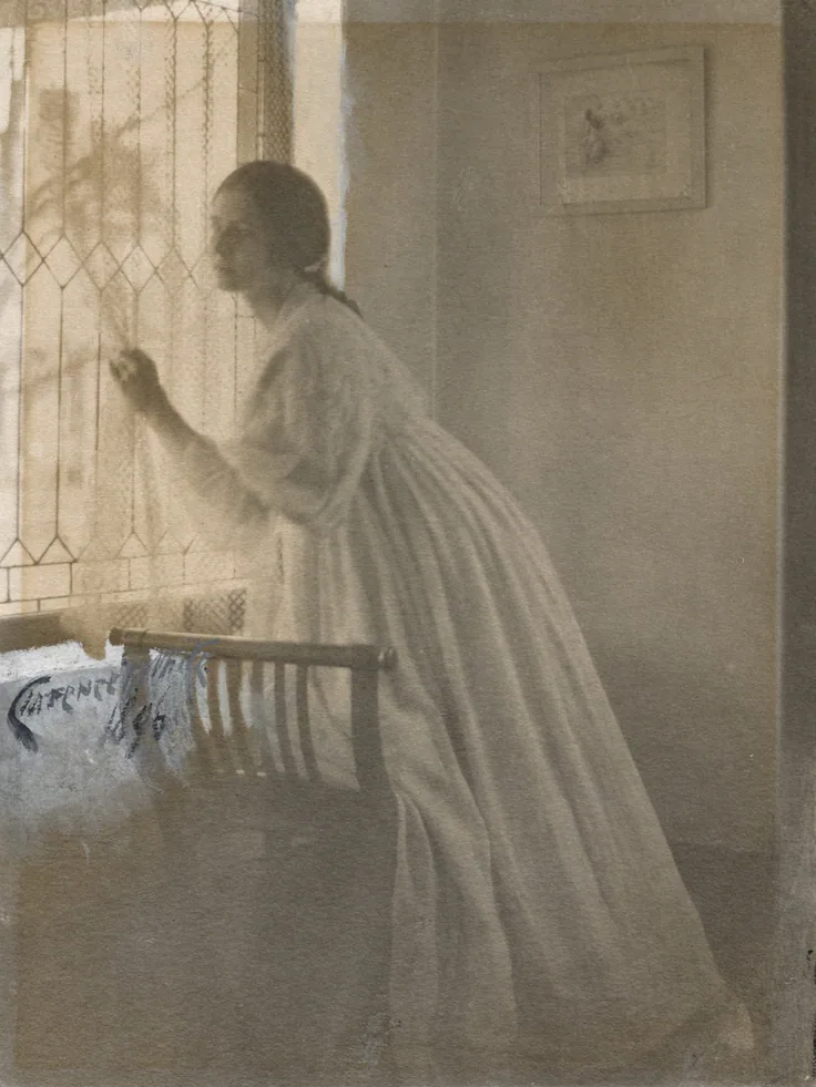 A woman in a pale gown leans to a leaded window, soft daylight dissolving the room into creamy greys.