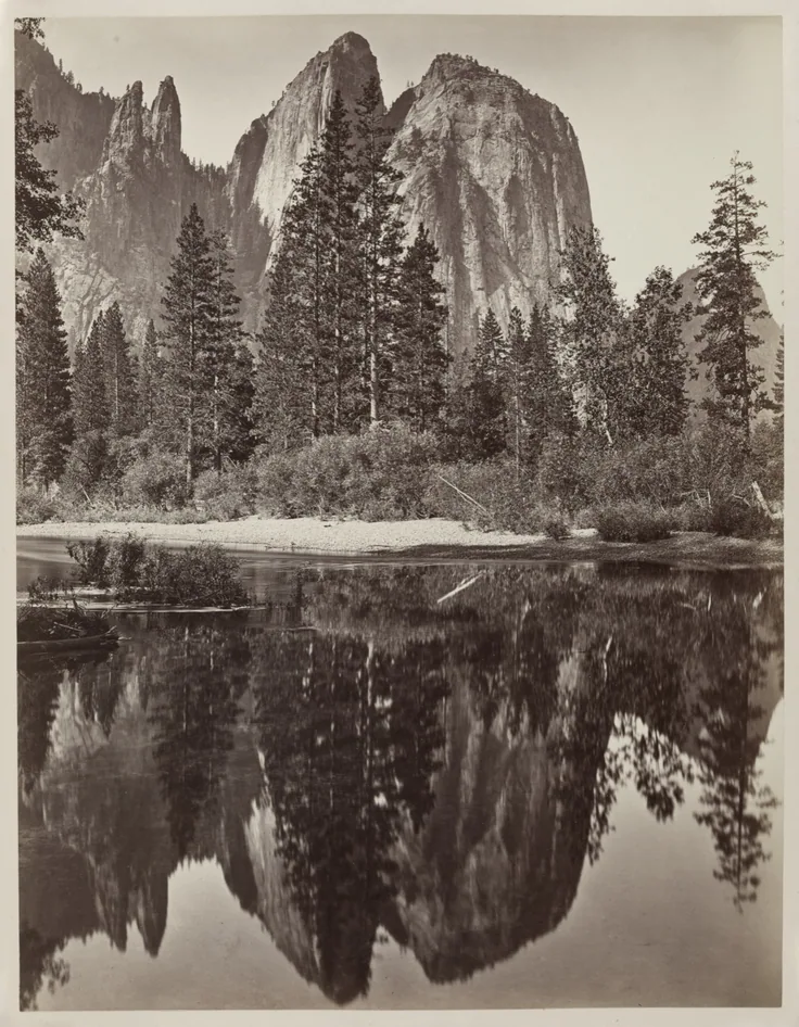 Granite spires and dark firs mirrored almost perfectly in a calm river, a pale sandbar between; crisp black and white.