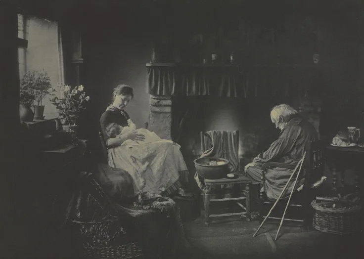 A mother holds a baby beside an old man warming himself at a cottage fire, window light on flowers; soft platinum greys.